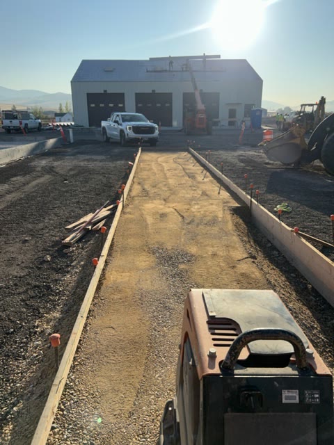 Formed sidewalk and curb subgrade runs toward a new shop building on a graveled site