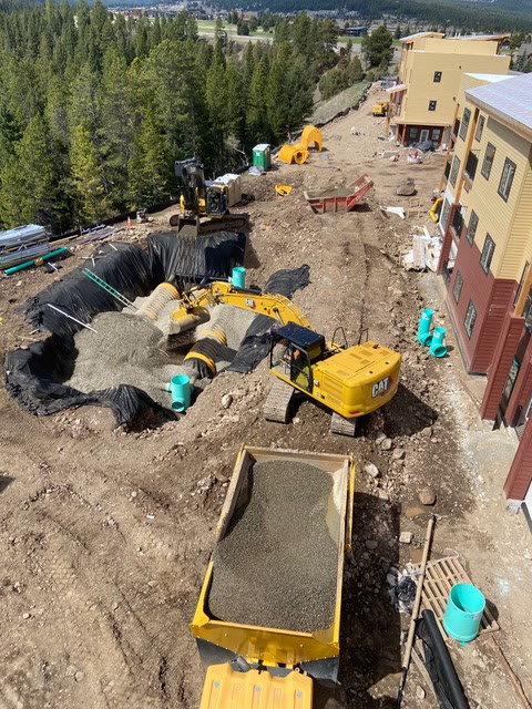 Excavators install a large underground stormwater detention system beside a multi-story building
