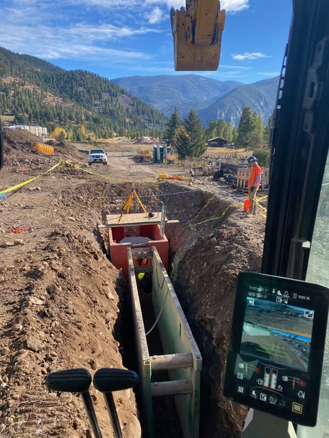View down a long shored pipe trench with mountain scenery beyond