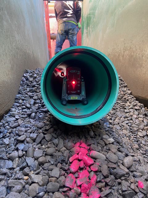 View through a green sewer pipe on gravel bedding with a pipe laser setting grade
